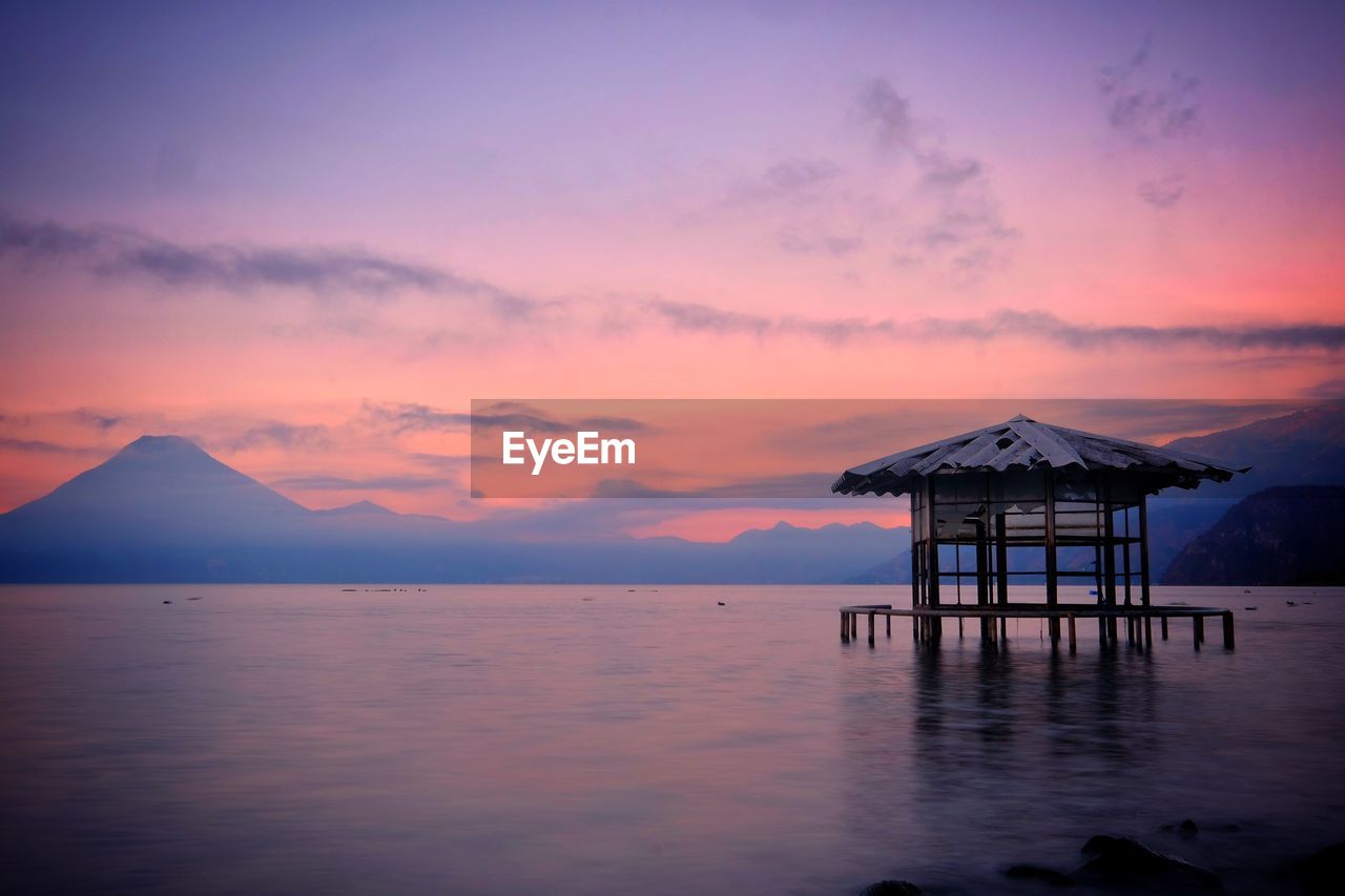 Lifeguard hut in sea against sky during sunset