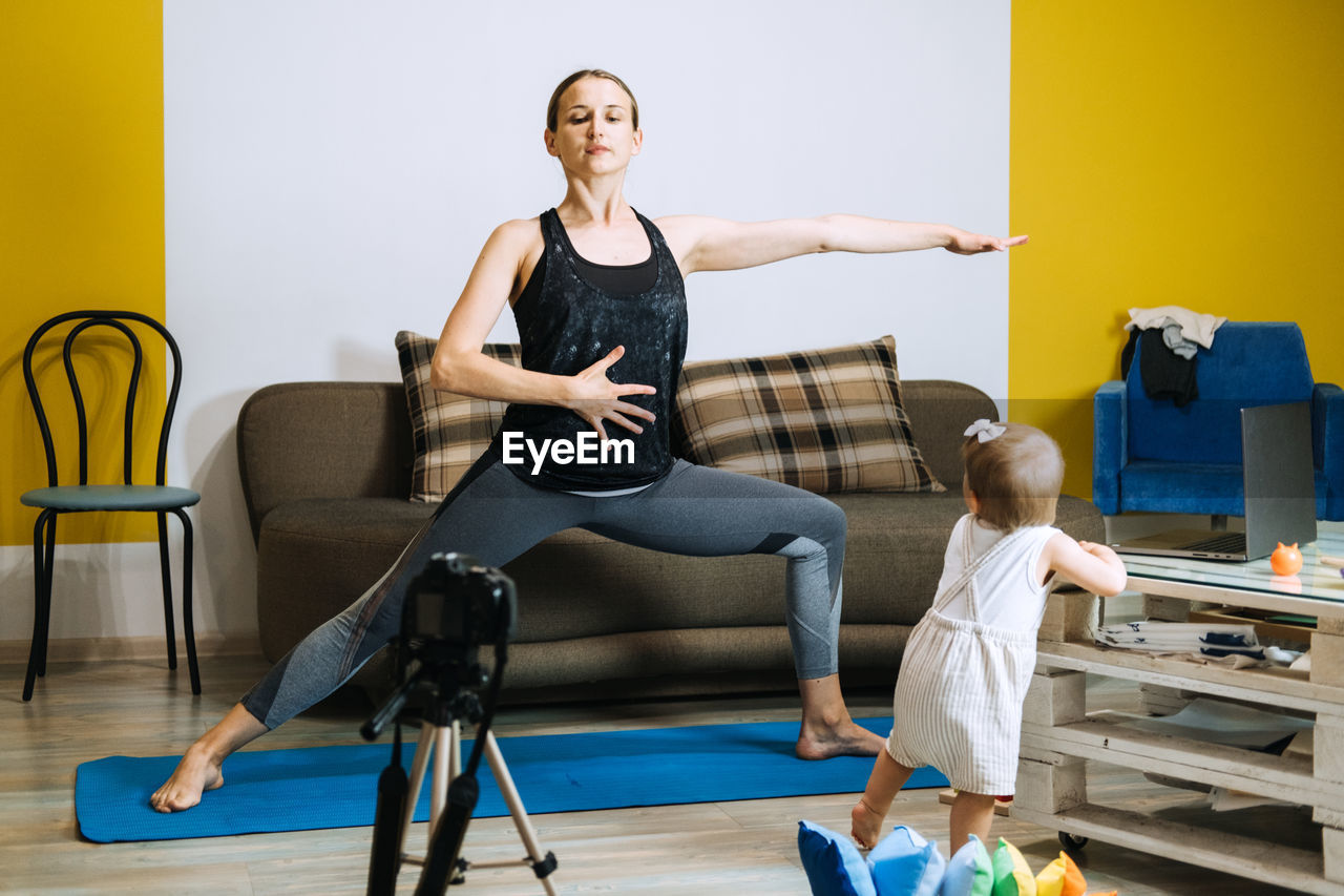 Young mother fitness instructor personal trainer record video near camera at home with baby