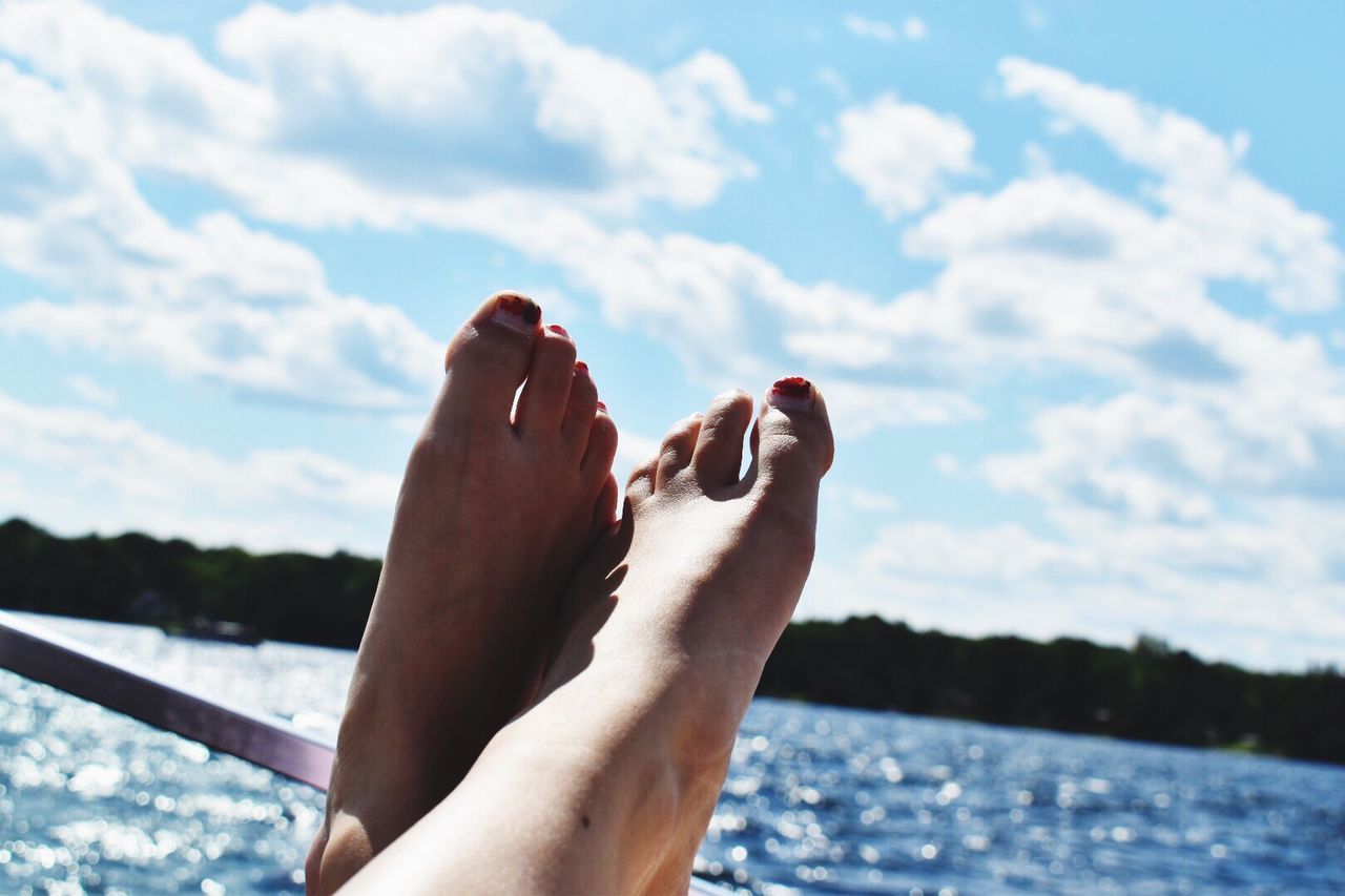 LOW SECTION OF MAN LEGS BY SEA AGAINST SKY