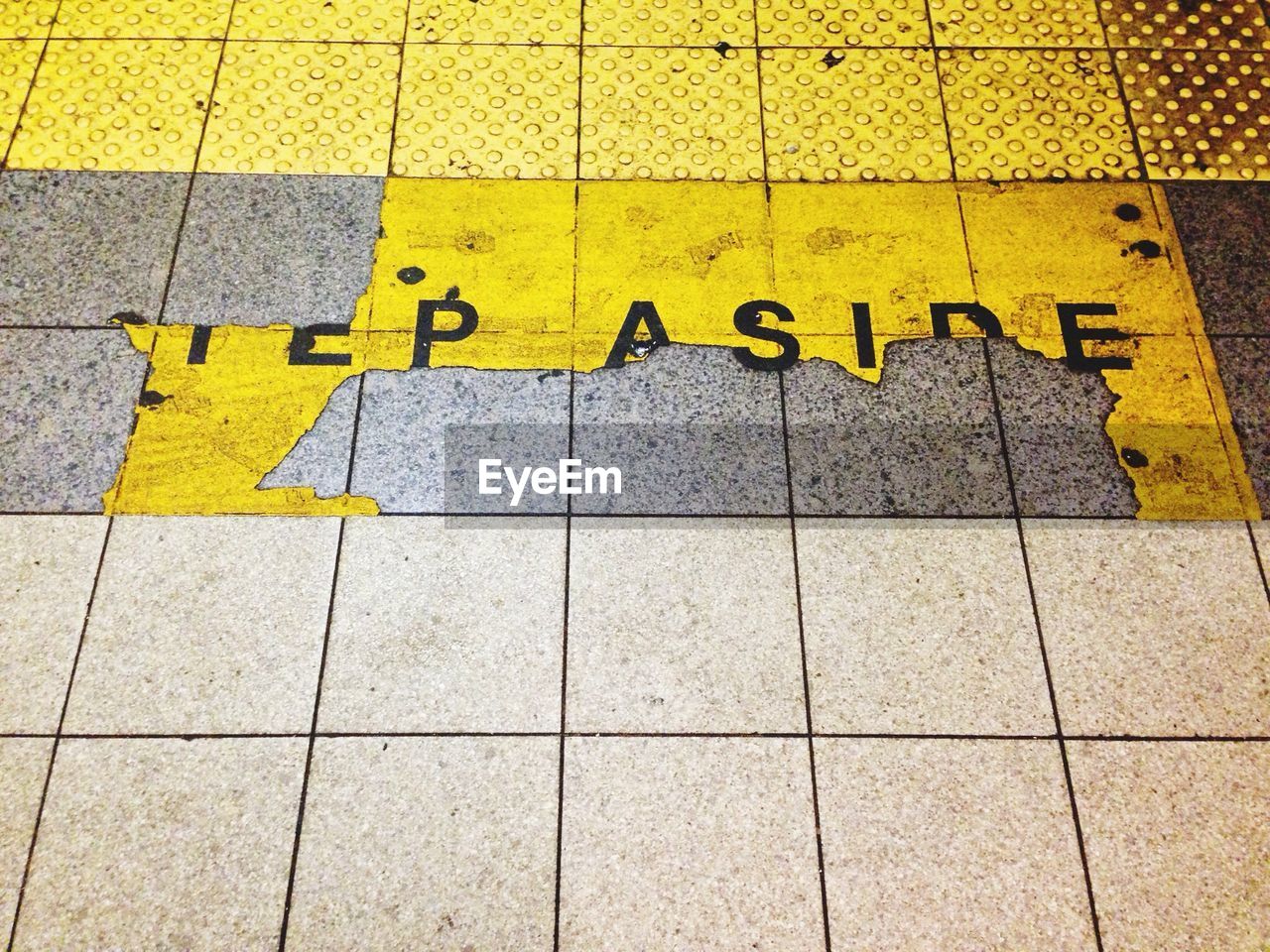 Close-up of damaged yellow text on tiled floor