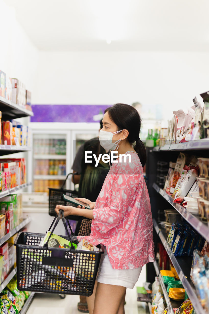 Asian woman with protective face mask with shopping basket in department store.