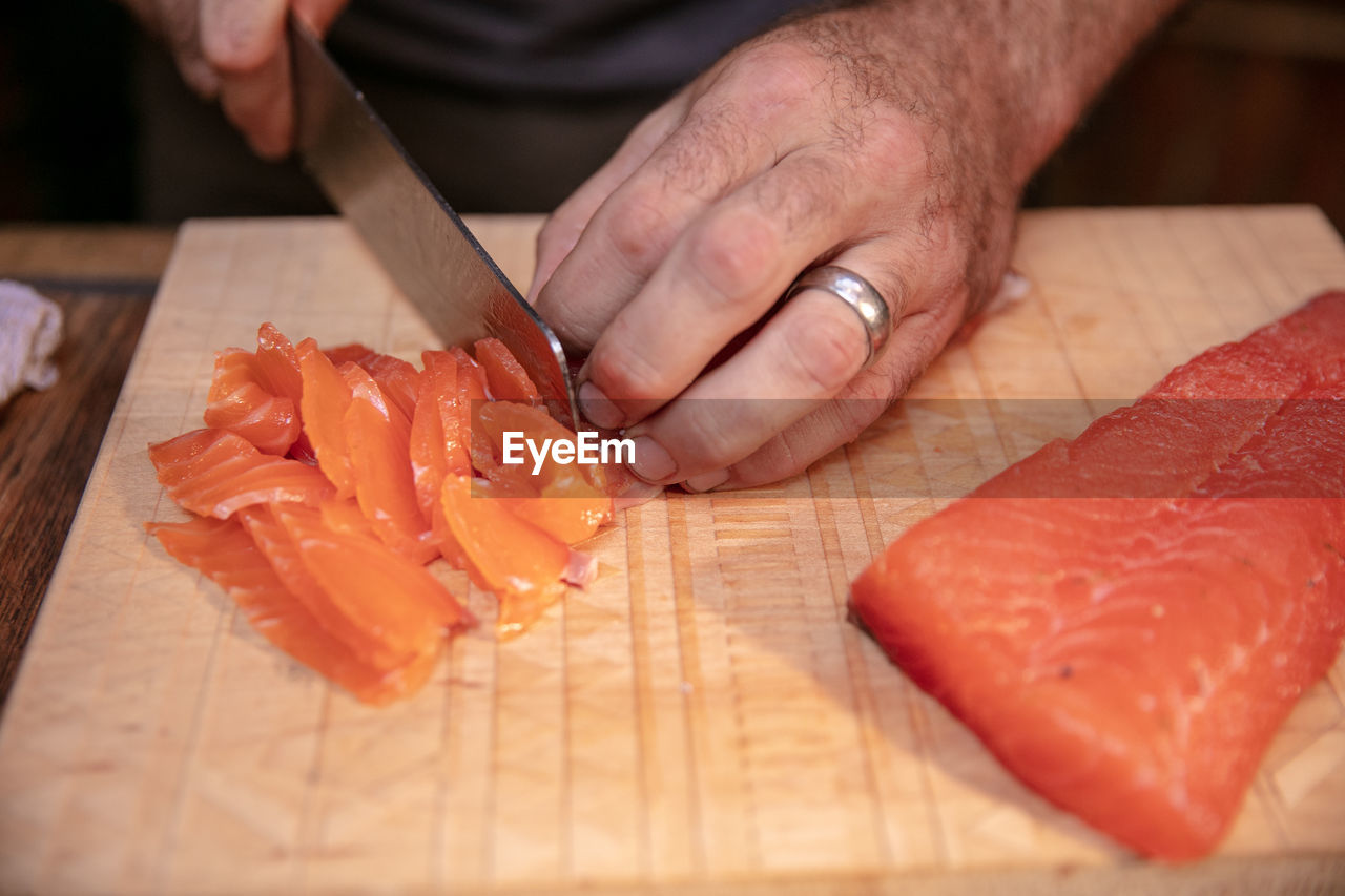 Cropped hands cutting salmon on cutting board