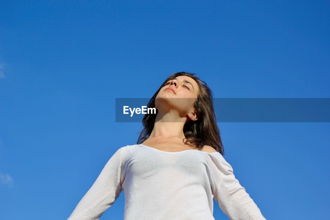 LOW ANGLE VIEW OF WOMAN LOOKING AT BLUE SKY AGAINST CLEAR BACKGROUND