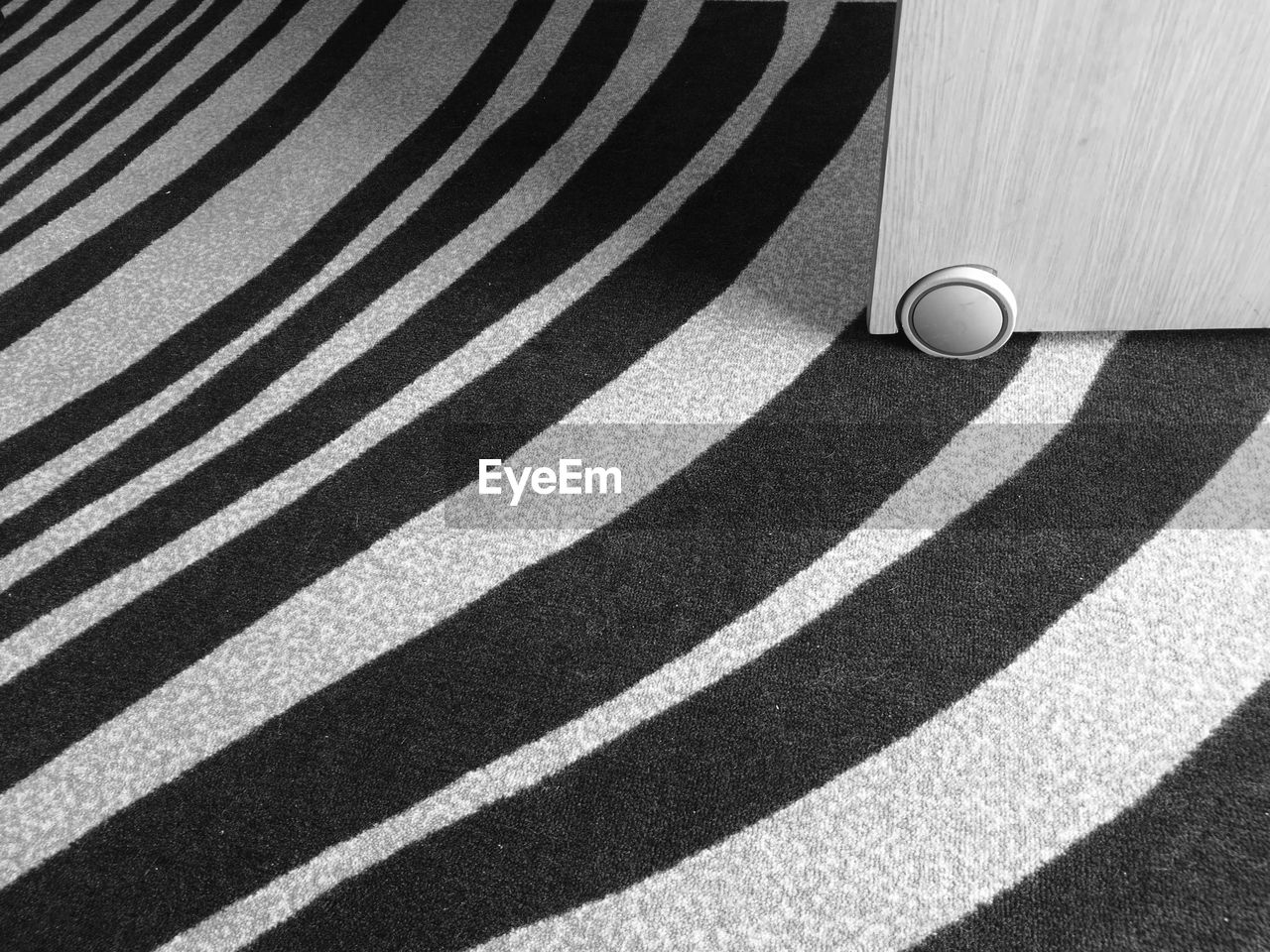 High angle view of a small wheel under a removable desk on a stripped carpet 