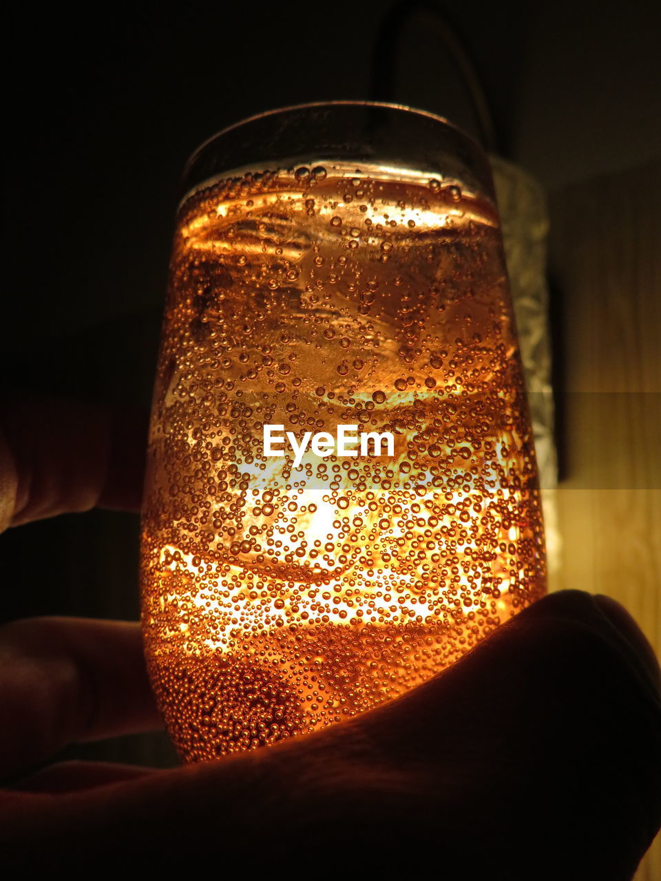 Close-up of hand holding glass against illuminated light