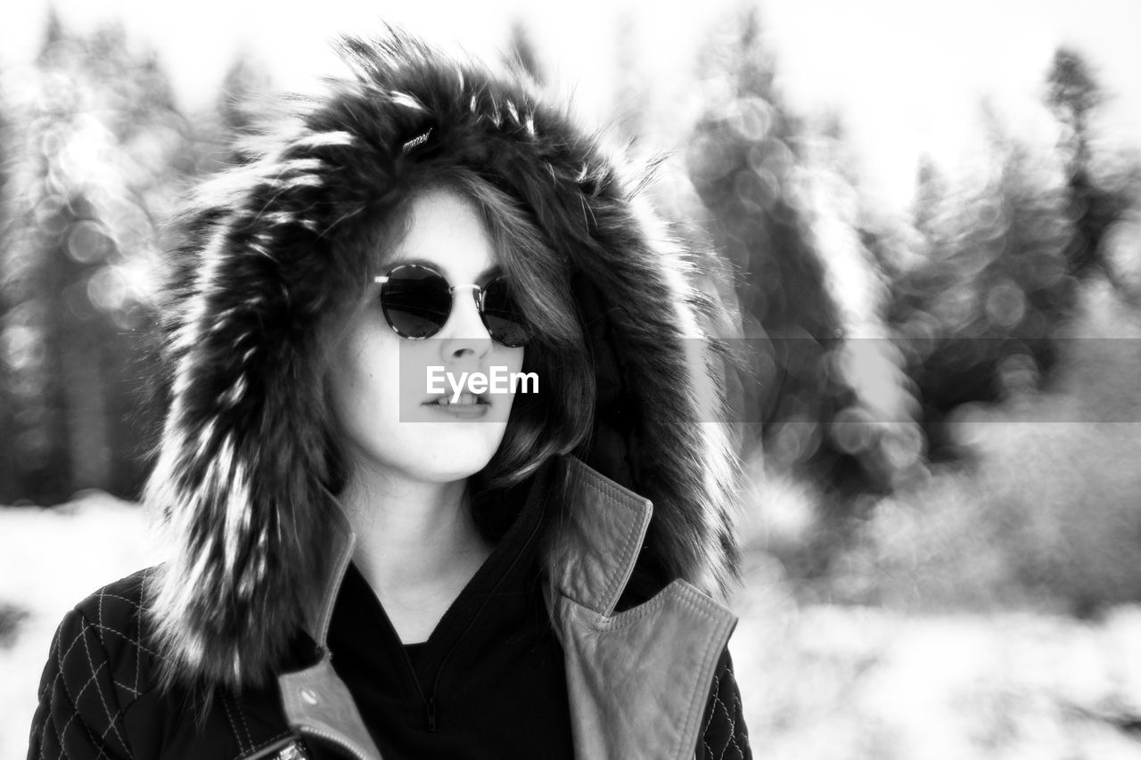 Woman wearing sunglasses standing against trees in winter