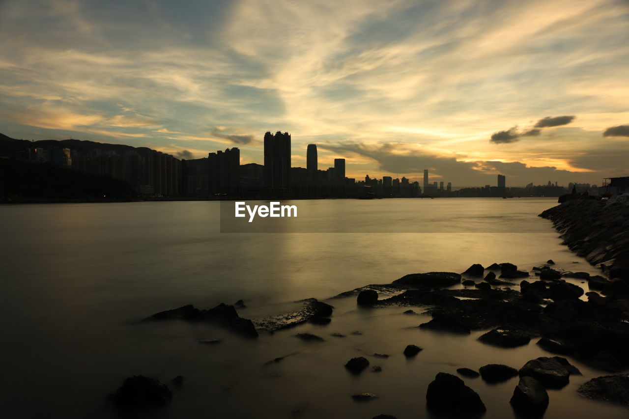 Sea by buildings against sky during sunset