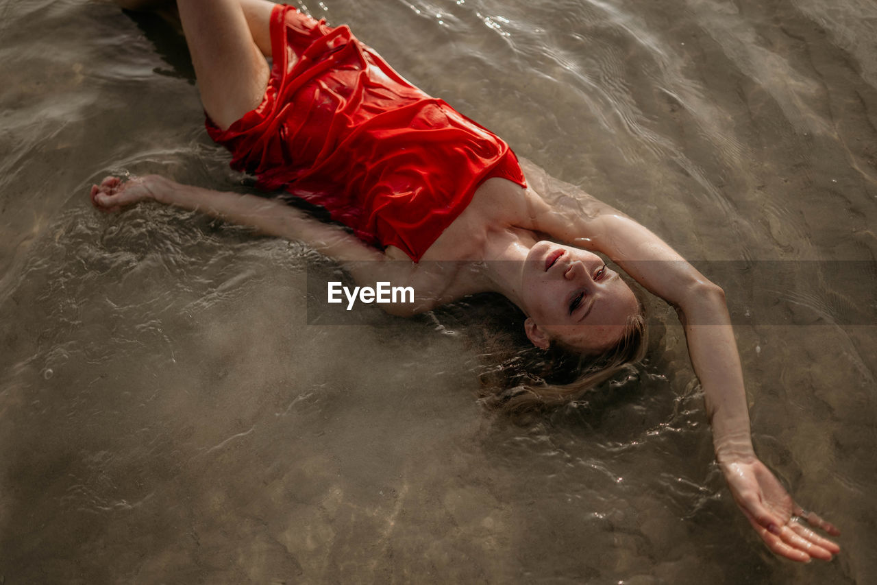 Girl in a red dress lies in sea water high angle