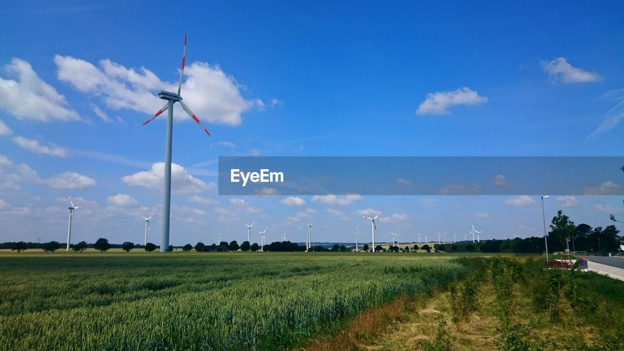 Wind turbines on field against cloudy sky