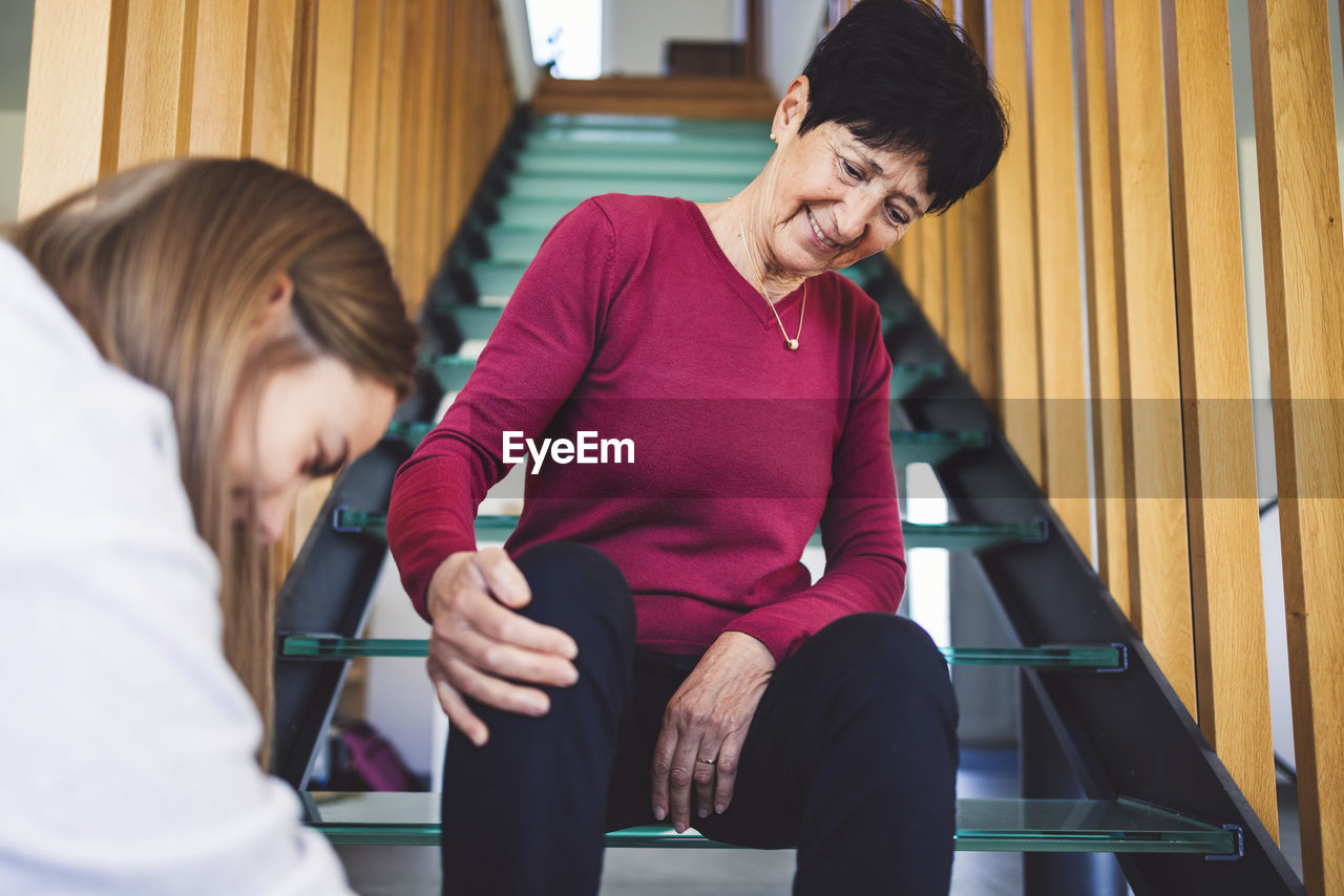 Senior woman sitting on the stairs patiently waiting for nurse to tie up her shoes