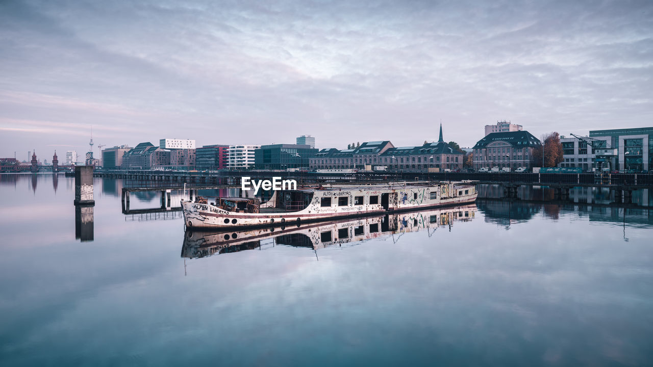 Boat moored on lake by buildings against sky 