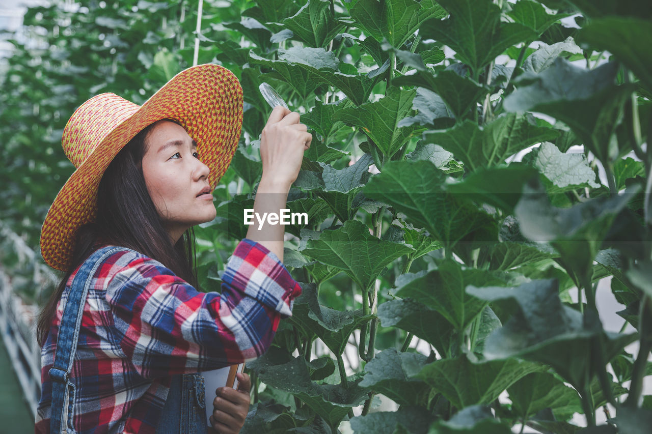 Woman standing by plants at greenhouse