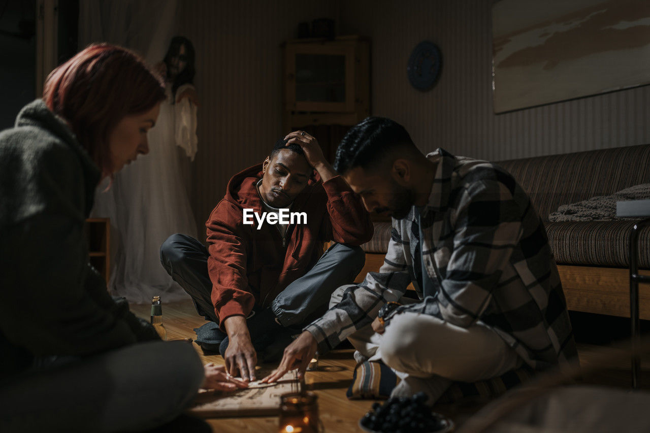 Friends touching ouija board while ghost in background at cabin