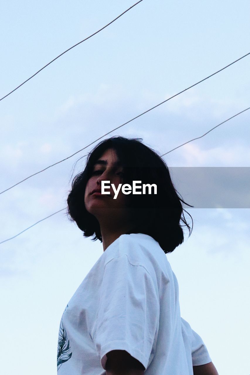 Low angle portrait of woman looking against sky