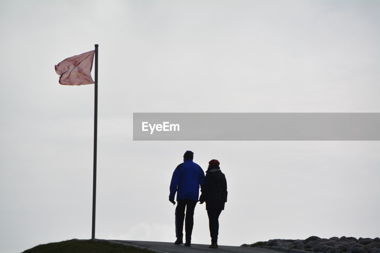 Rear view of couple walking by flag against sky
