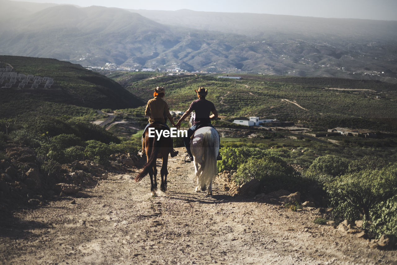 People riding horses on mountain road against sky