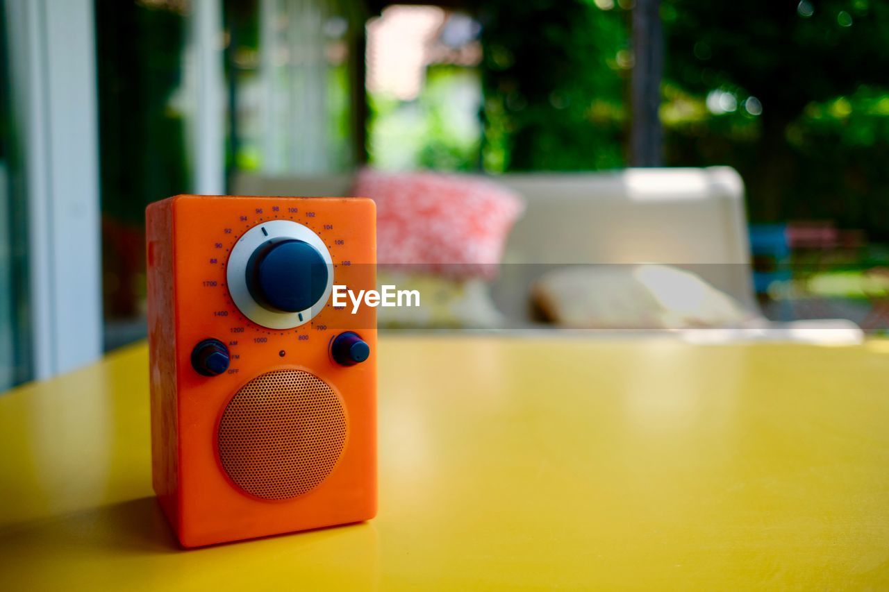 Close-up of orange radio on yellow table