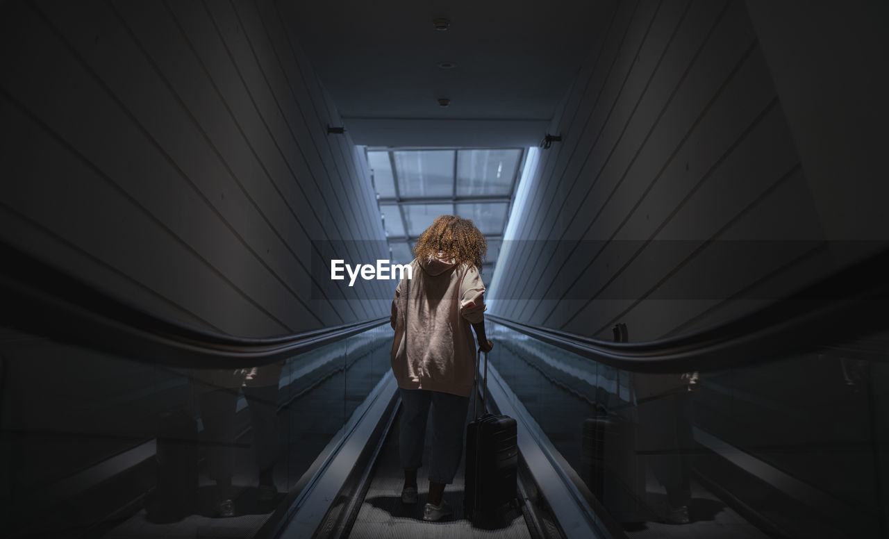 Young woman holding suitcase standing on escalator at airport