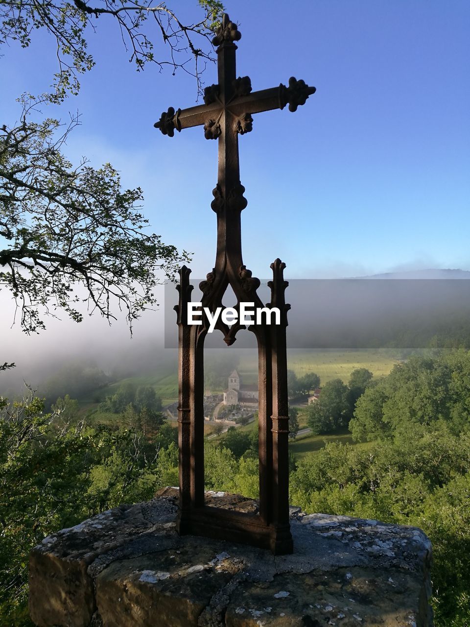 View of cross on stone structure overlooking trees and mountains against sky