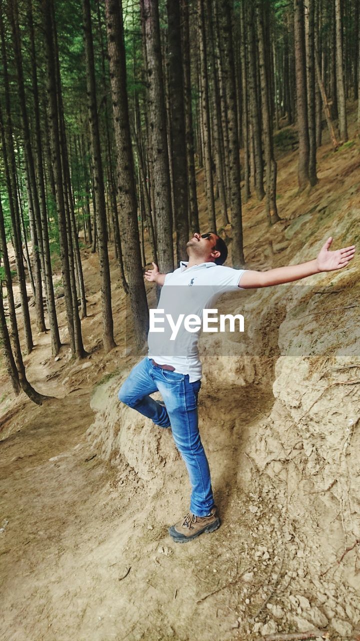 MAN STANDING ON TREE TRUNK IN FOREST