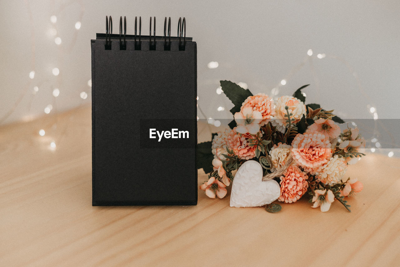 Notebook  with copy space, on a wooden table with a bouquet and a heart and bokeh lights