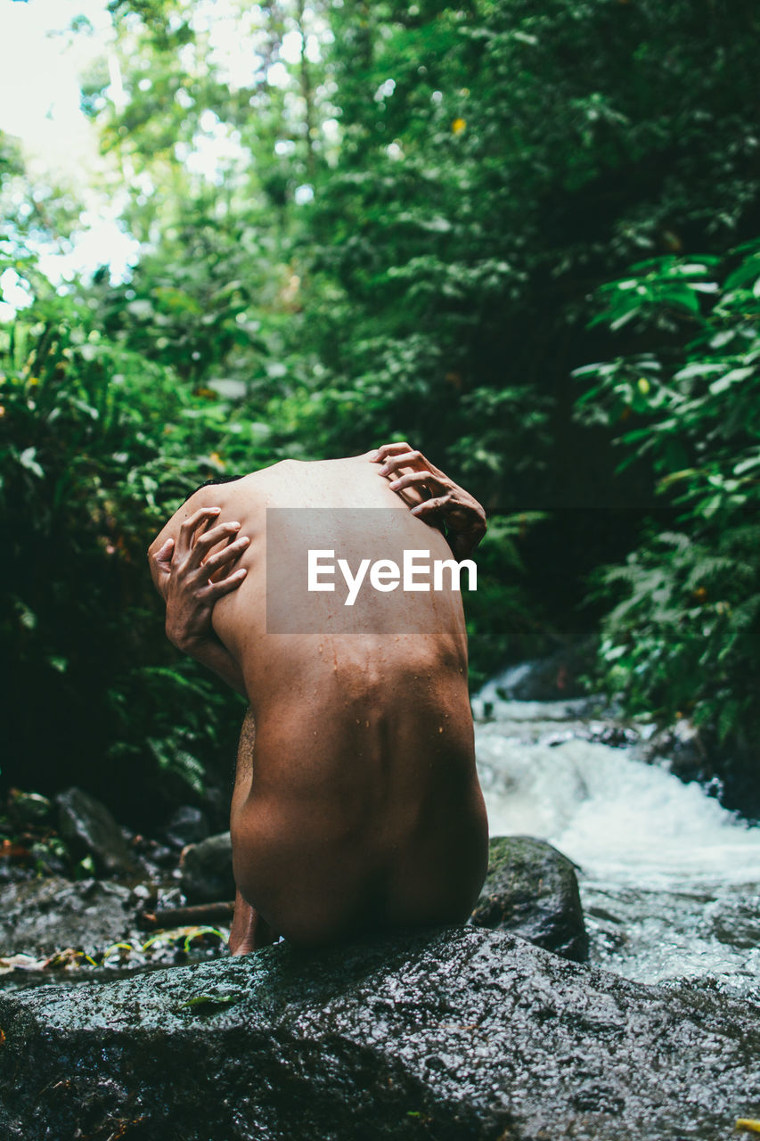 Rear view of naked man sitting by river