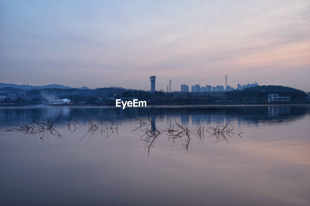 Scenic view of lake by buildings against sky during sunset