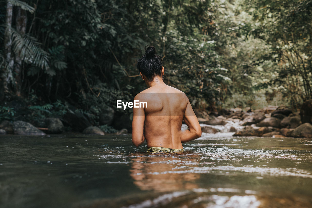 REAR VIEW OF SHIRTLESS MAN STANDING IN WATER