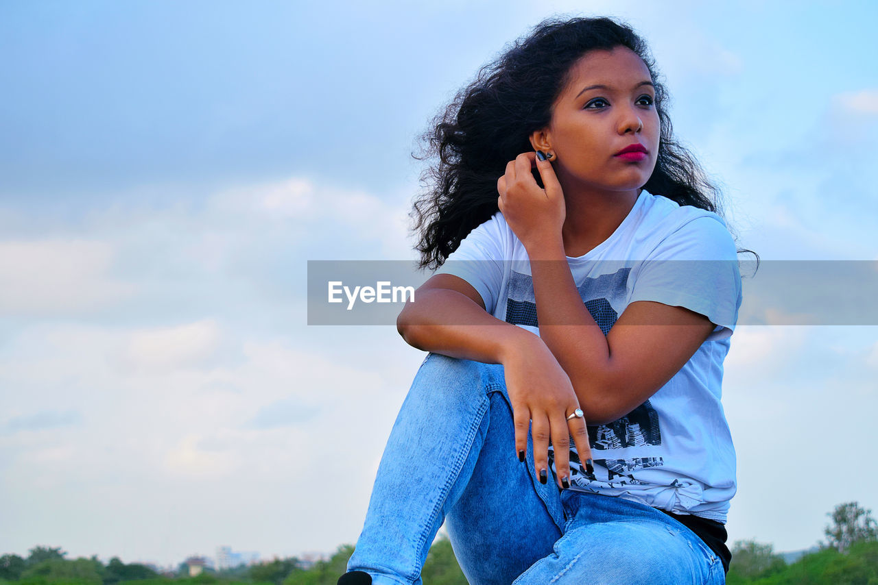 PORTRAIT OF A WOMAN SITTING AGAINST SKY