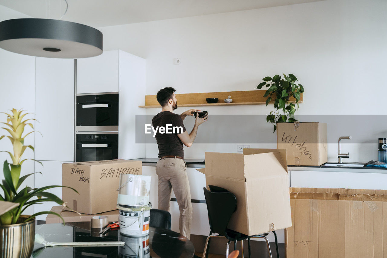 Man arranging bowls on shelf while standing in kitchen at new home