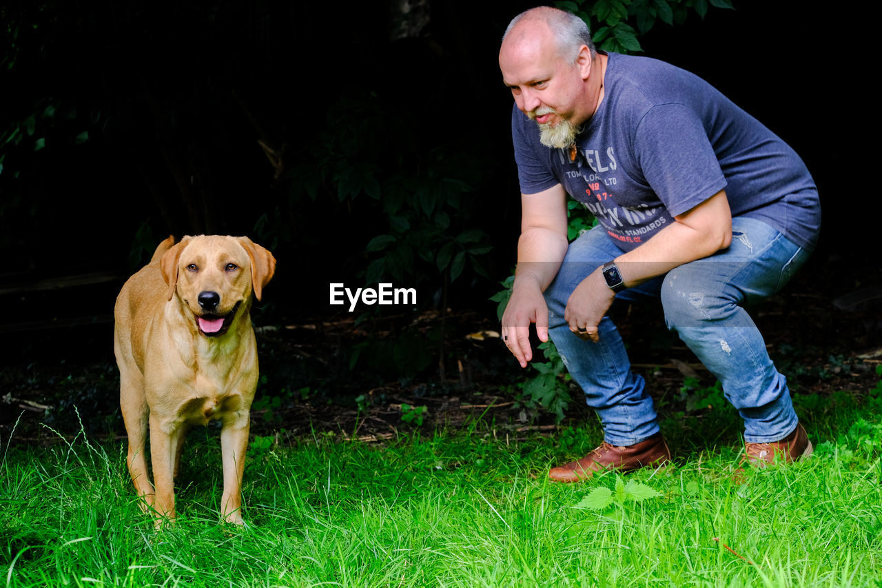 Full length of man and dog looking at grass