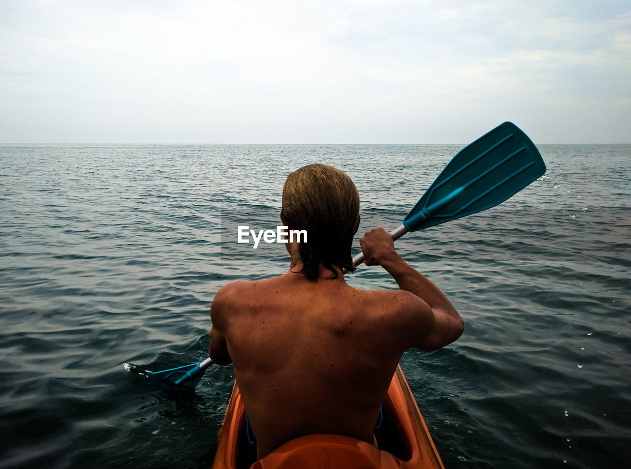 Rear view of shirtless man kayaking in sea against sky