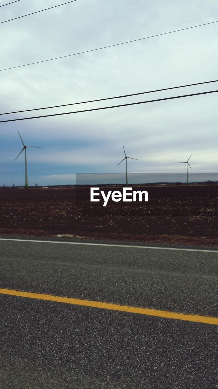 Wind turbines on field by road against cloudy sky