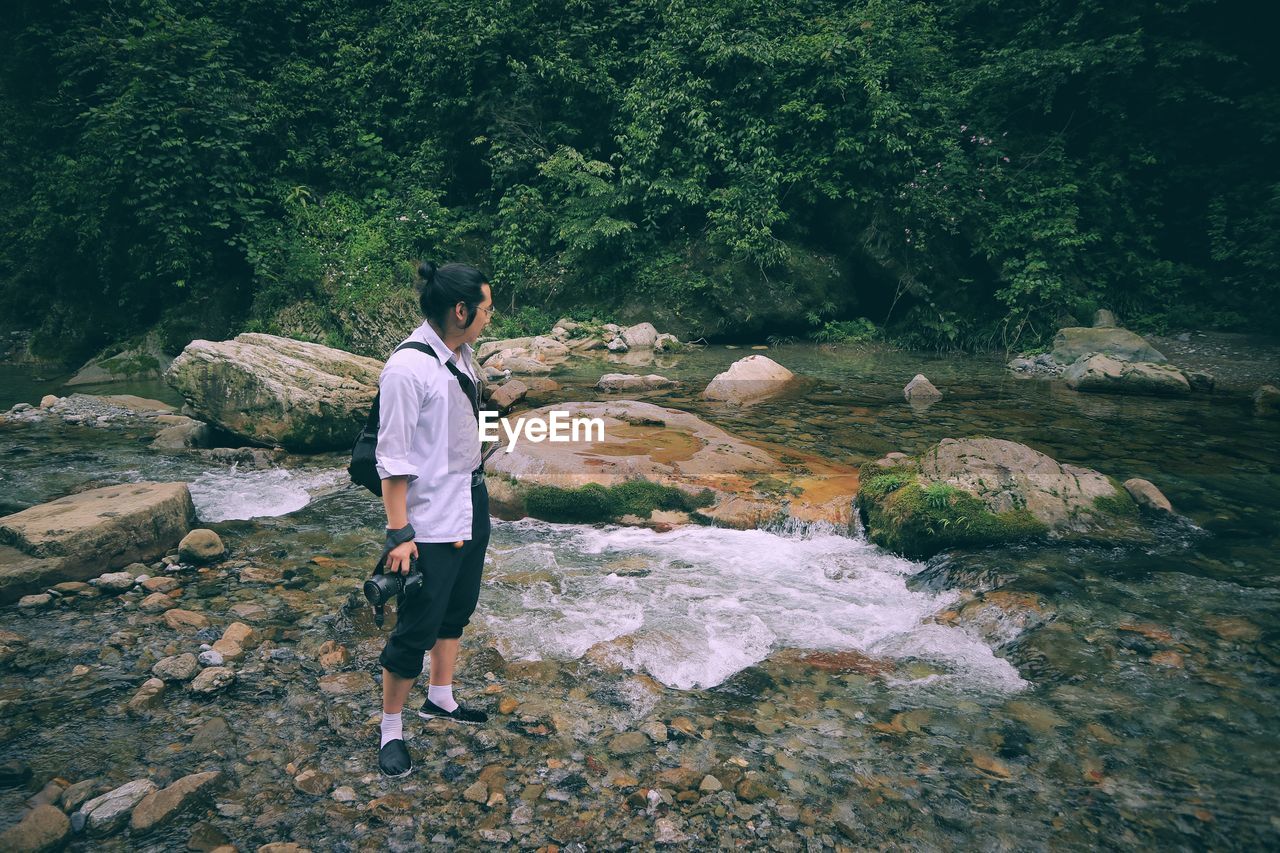 REAR VIEW OF MAN STANDING ON ROCK AT SHORE