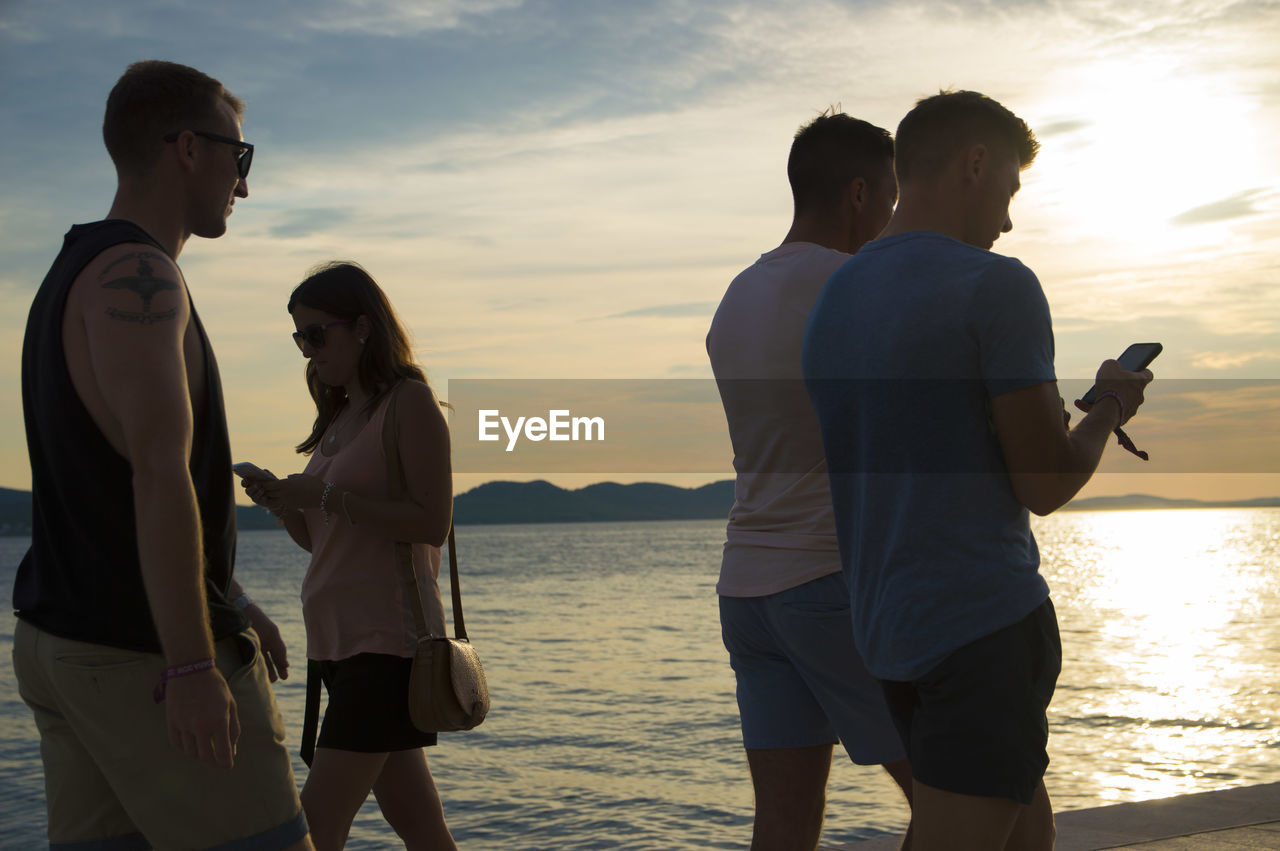 REAR VIEW OF FRIENDS STANDING ON BEACH