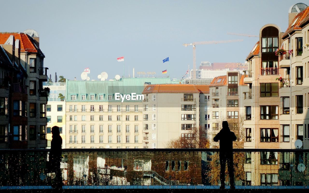 Silhouette people standing by railing in city against sky