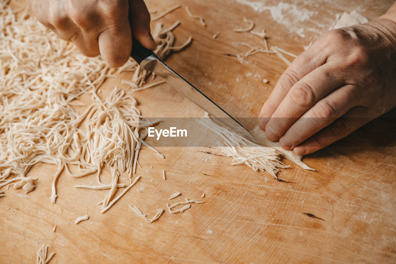 A woman cuts the dough with a knife and makes homemade noodles in the kitchen.
