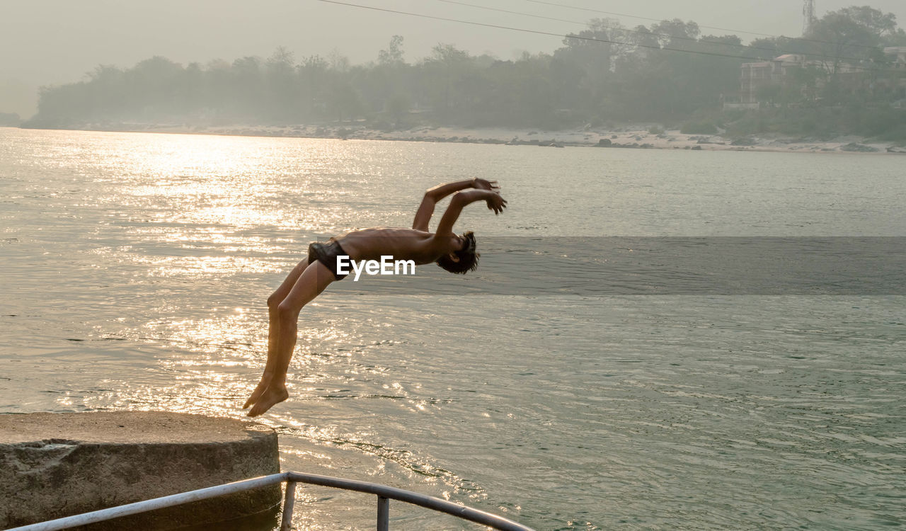 Full length of shirtless man jumping in river