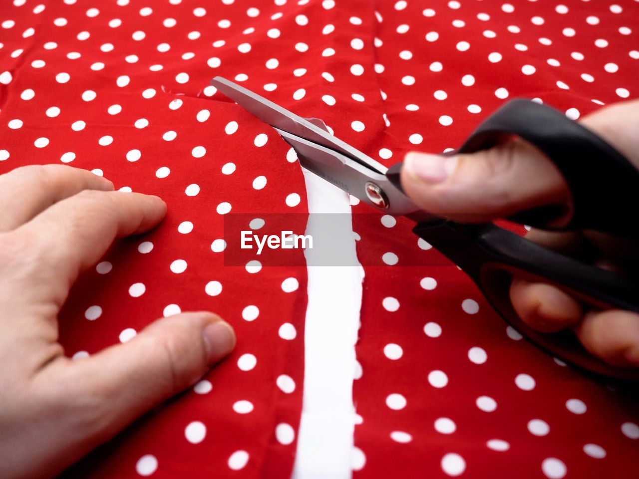 Cropped hands cutting red fabric at table