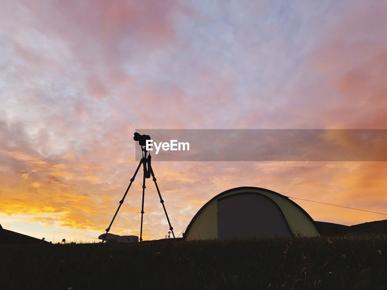 Tents and tripod on field against sky during sunset