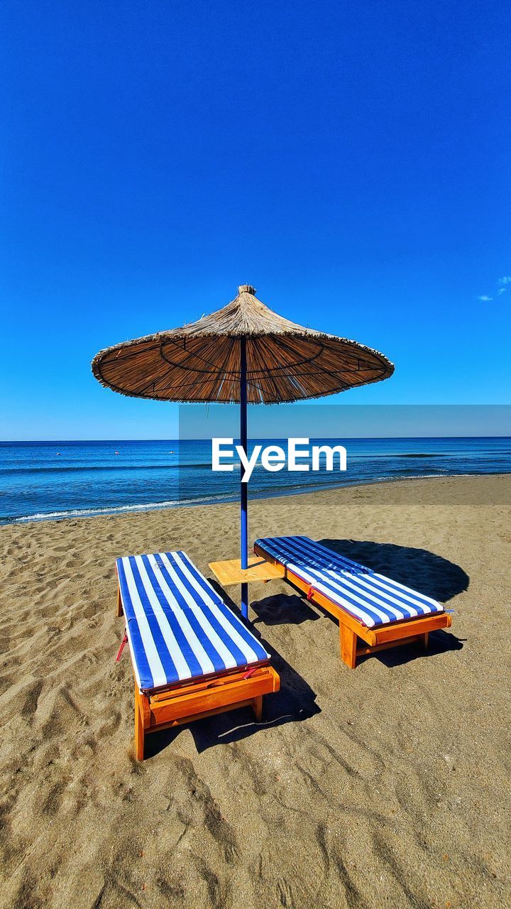 Deck chairs on beach against clear blue sky