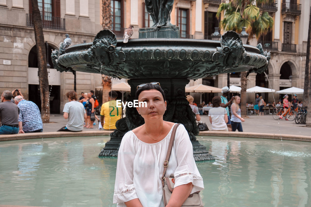 Woman sitting against fountain in city