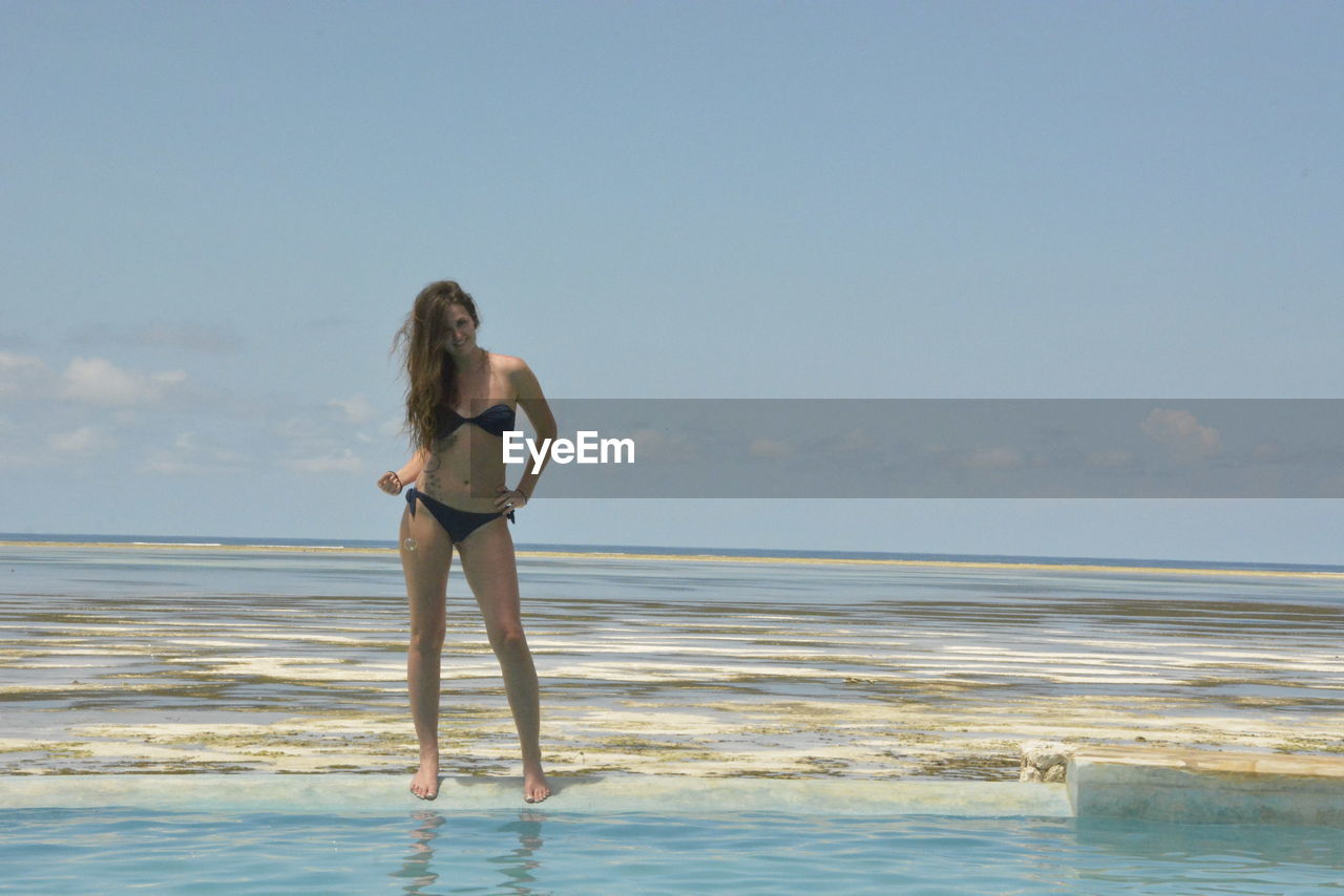 WOMAN STANDING ON BEACH AGAINST SKY