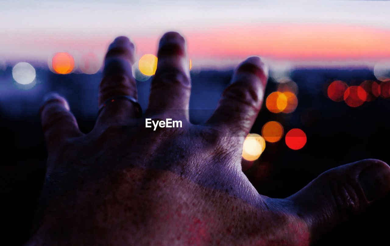 Close-up of hand against sky during sunset