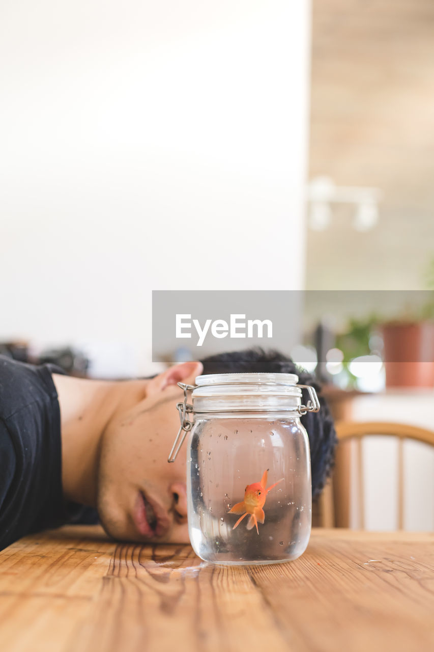 Young man with goldfish in jar on table at home