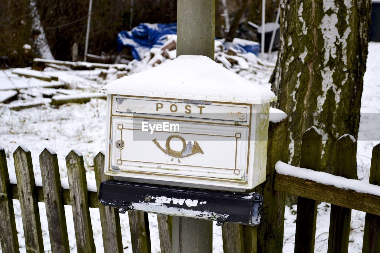 Snow on old post box with text on fence during winter