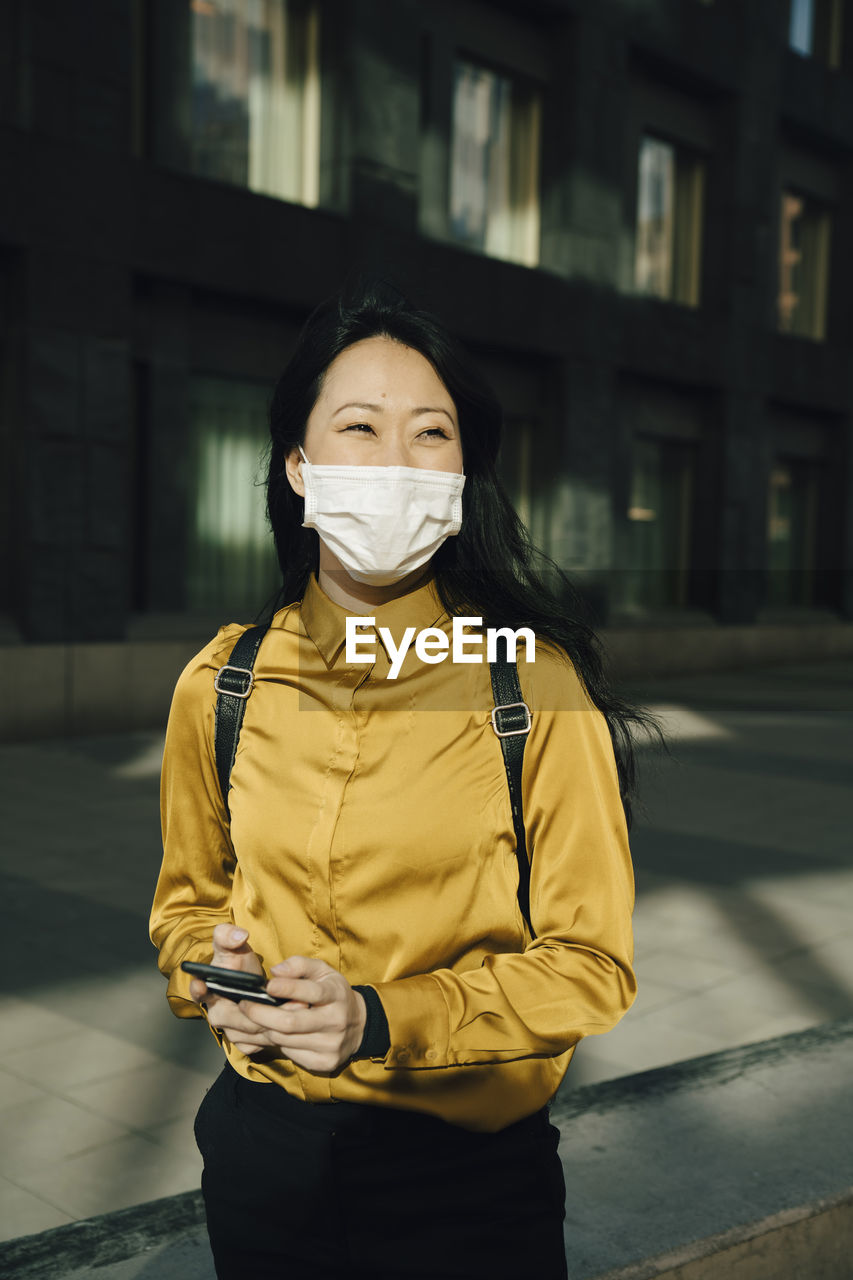 Happy woman with face mask holding smartphone