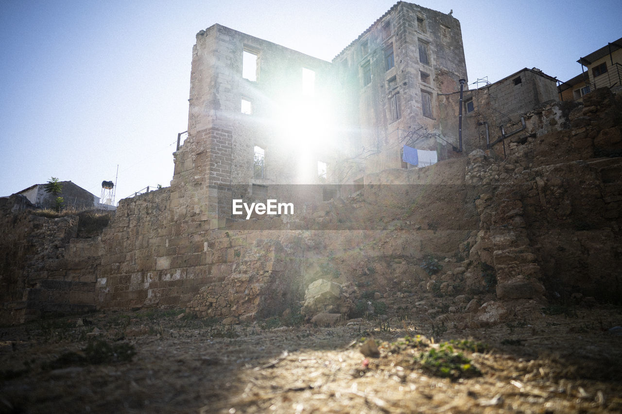 architecture, sky, built structure, lens flare, nature, ruins, building exterior, history, sunlight, clear sky, building, wall, low angle view, sunbeam, the past, no people, rock, old ruin, terrain, ancient history, sun, sunny, outdoors, fortification, city, castle, travel, old, day