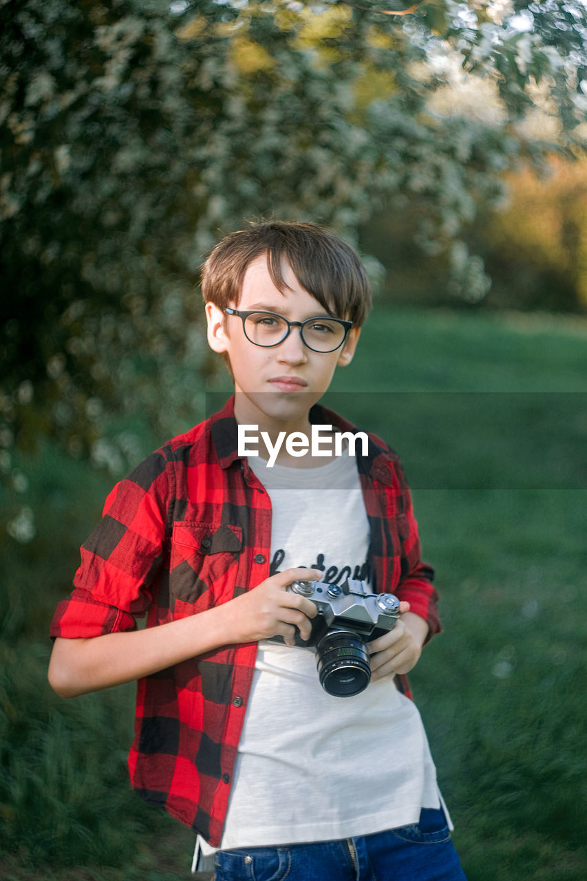 Portrait of boy holding camera while standing outdoors