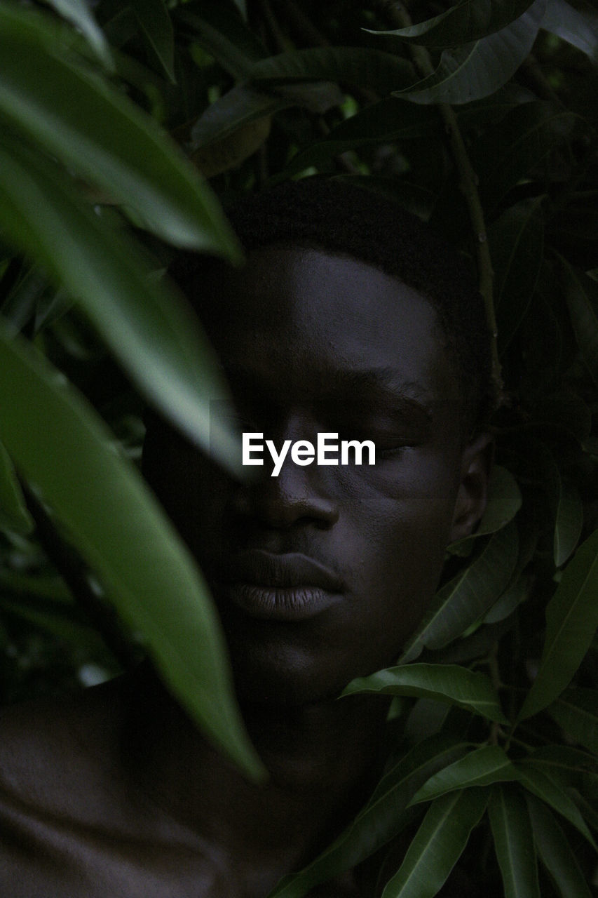 Close-up of young man with eyes closed amidst plants in forest